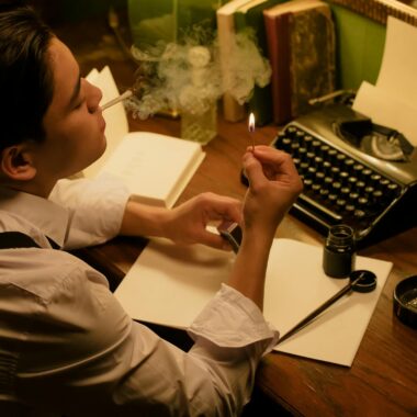 A man writing with a typewriter in a dimly lit room, smoking and concentrating on his work.